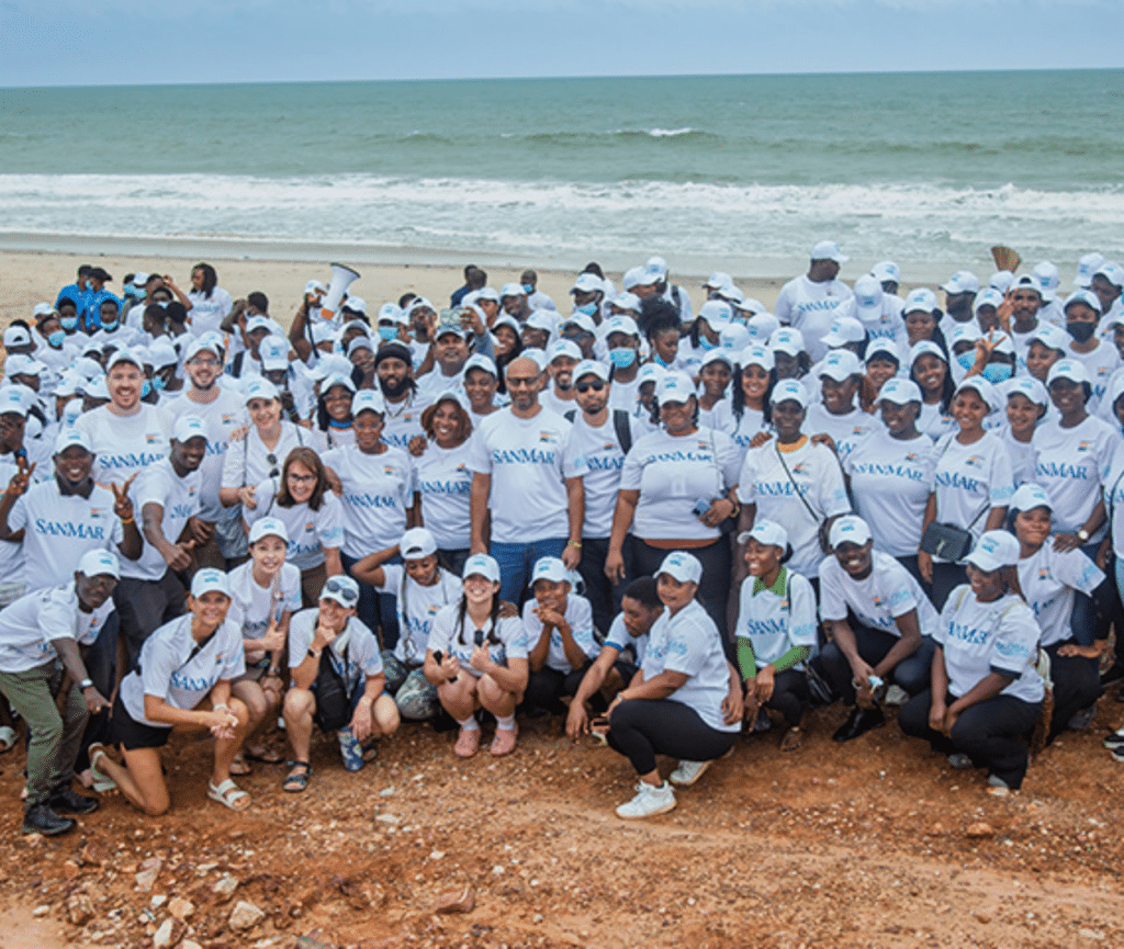 Corporate volunteer team wearing white SANMAR logo shirts posing on the shoreline