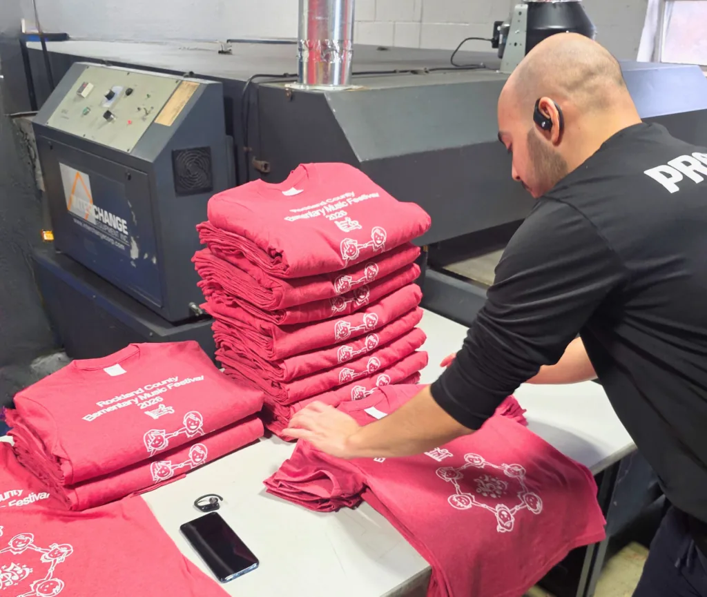 Worker folding stacks of custom printed red t-shirts in production facility.