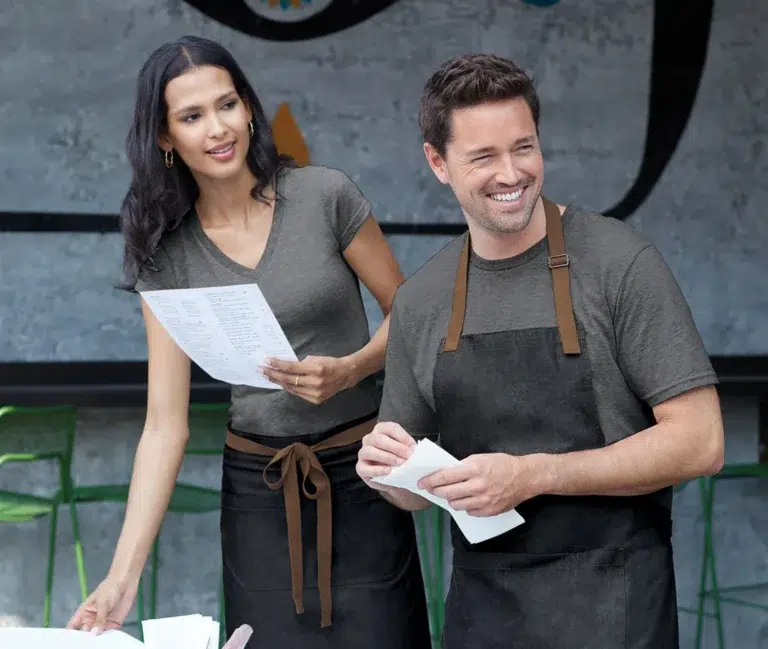Restaurant staff wearing custom T-shirts and aprons reviewing orders, suitable for hospitality uniforms