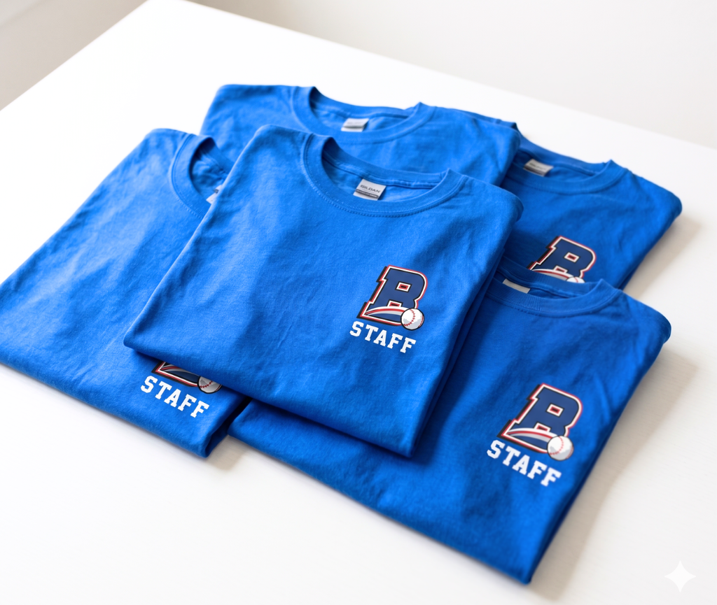 Stack of custom blue staff t-shirts with printed baseball team logos, prepared for event staff uniforms and team apparel.